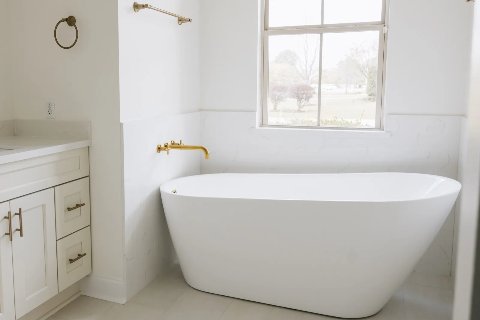 Primary bathroom wide view — freestanding tub, vanity with brass sconces, marble tile