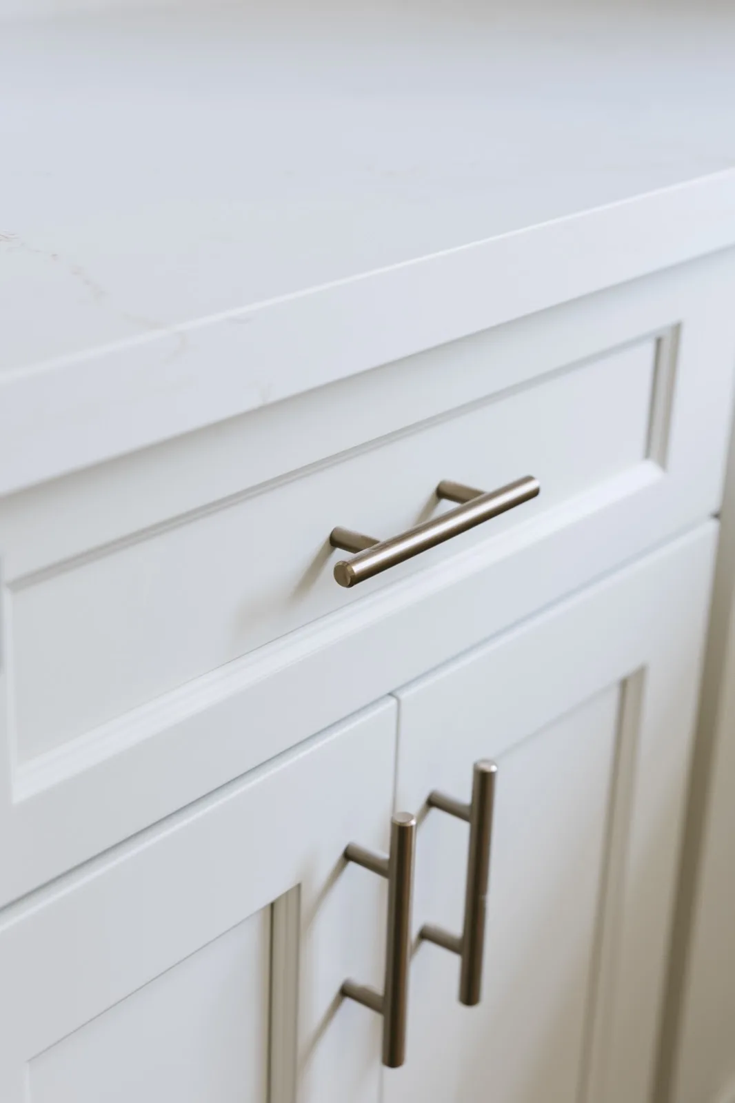 Brushed brass cabinet pull on white shaker drawer — quartz countertop above