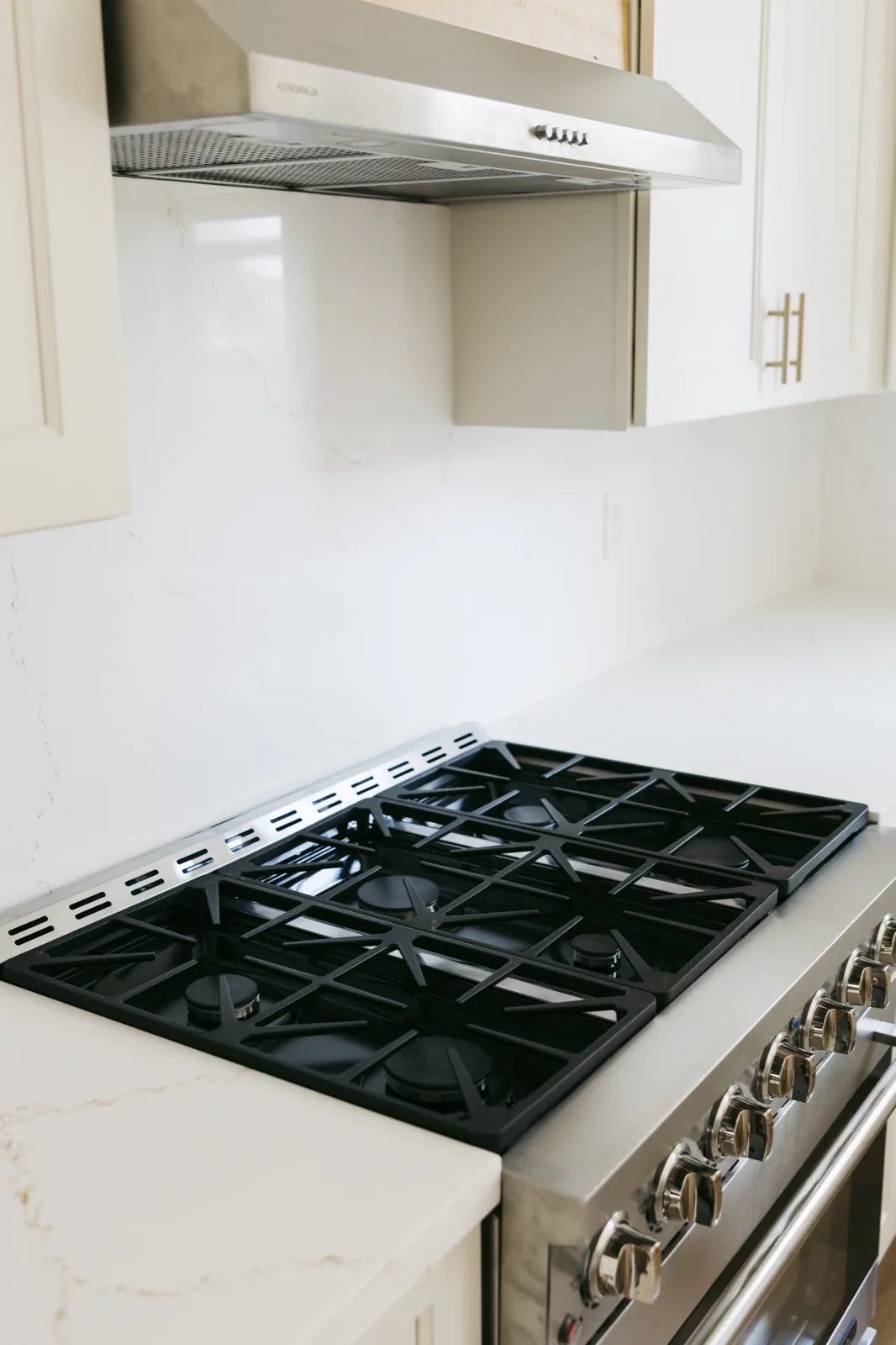 6-burner gas cooktop close-up with quartz backsplash and stainless hood
