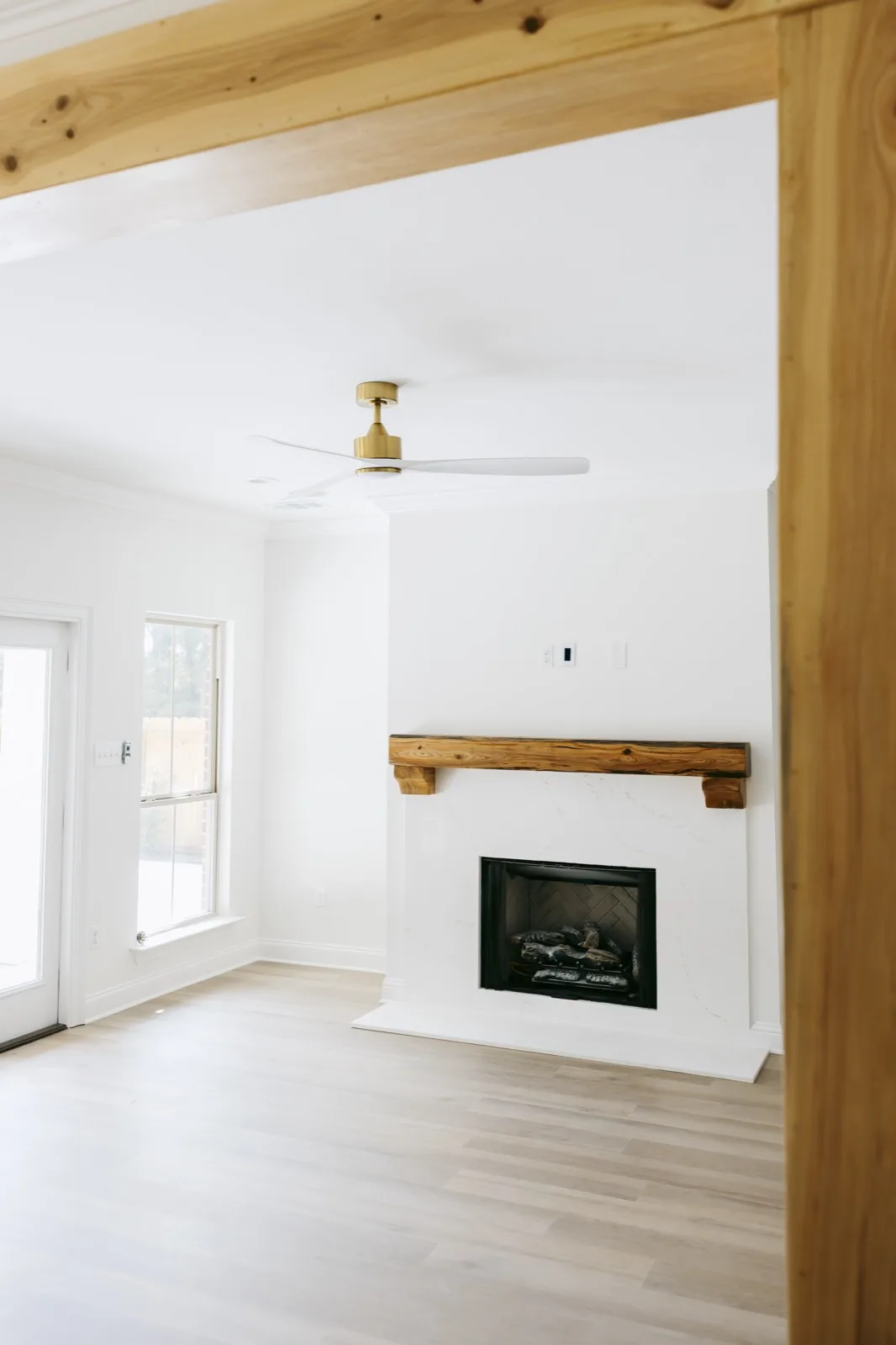 Fireplace from alternate angle — rustic mantel, modern ceiling fan, glass door to exterior