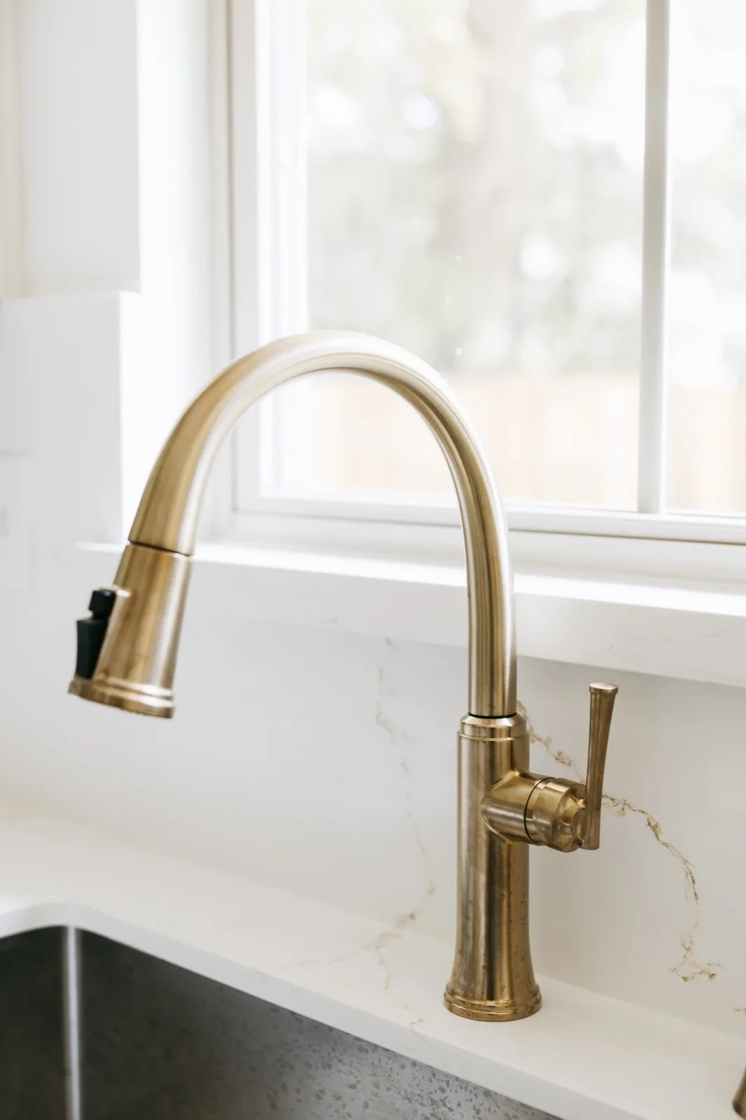 Gold gooseneck pull-down kitchen faucet against quartz backsplash