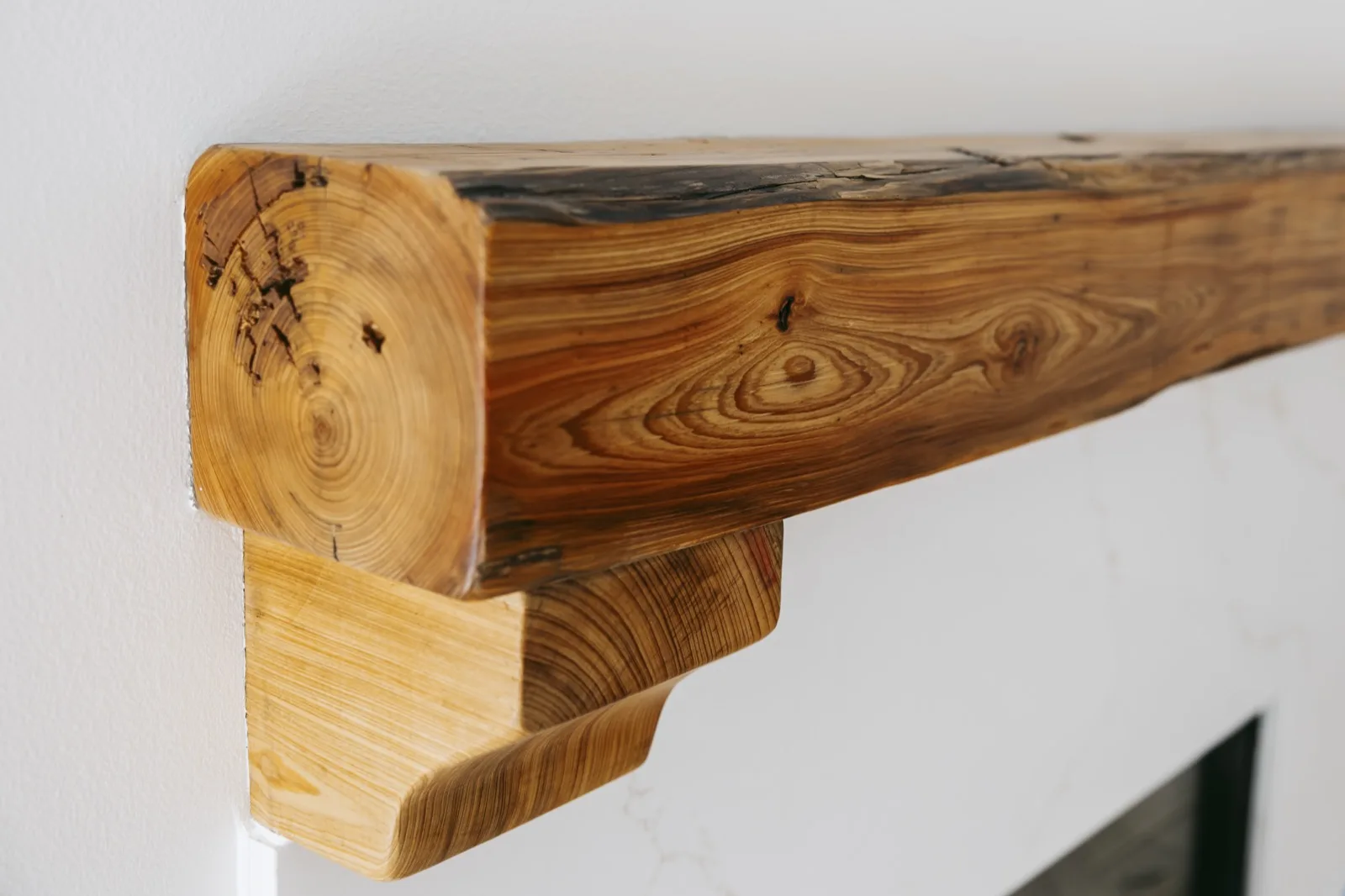 Live-edge cypress mantel — right side corbel detail showing wood grain rings and hand-carved bracket