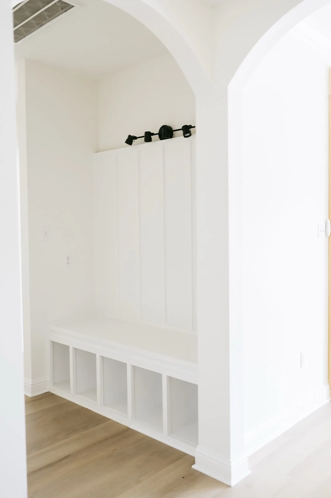 Mudroom through arched doorway — bench with cubbies and board-and-batten under archway