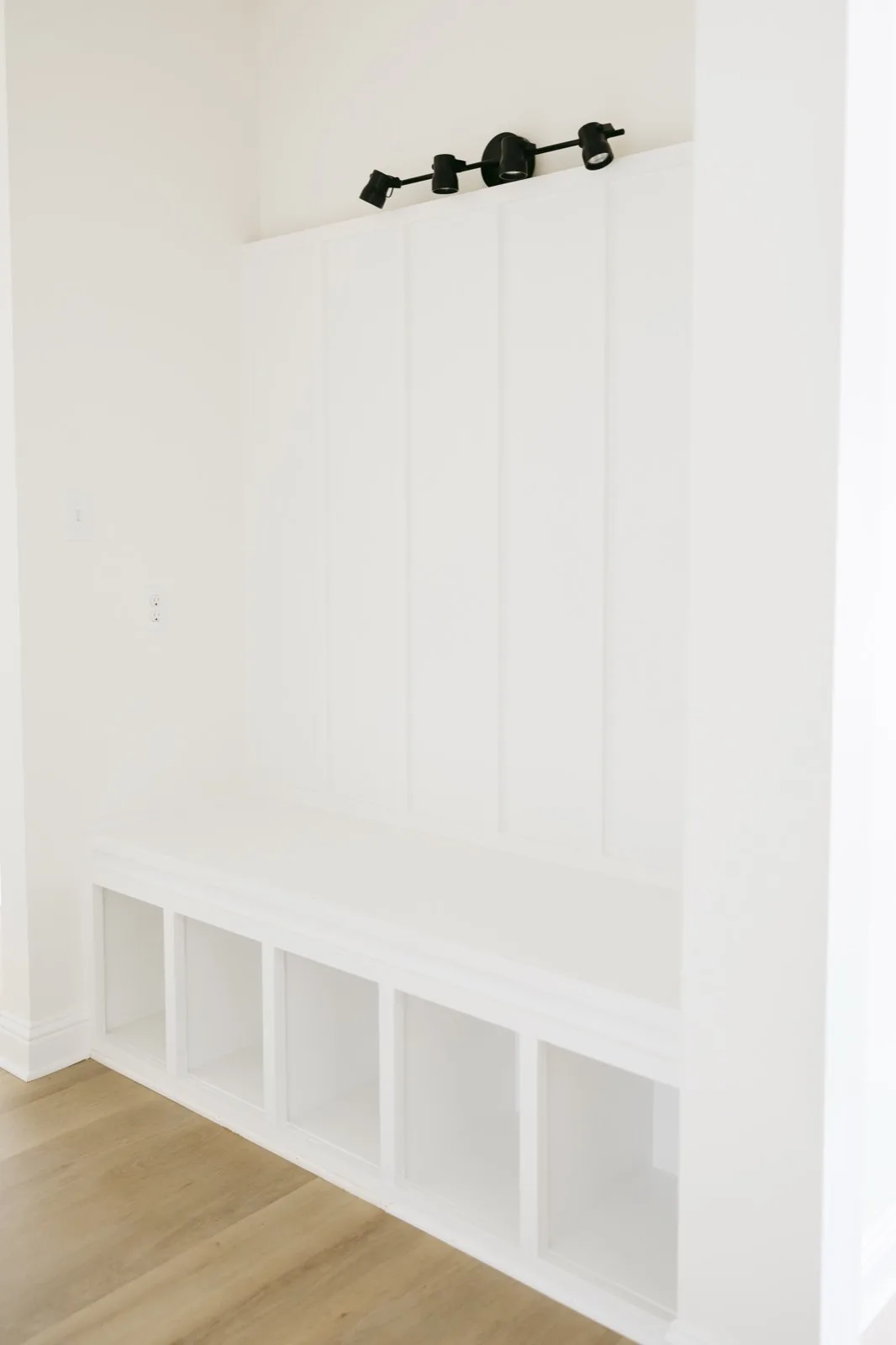 Mudroom bench nook straight on — board-and-batten wall, cubby storage, track light
