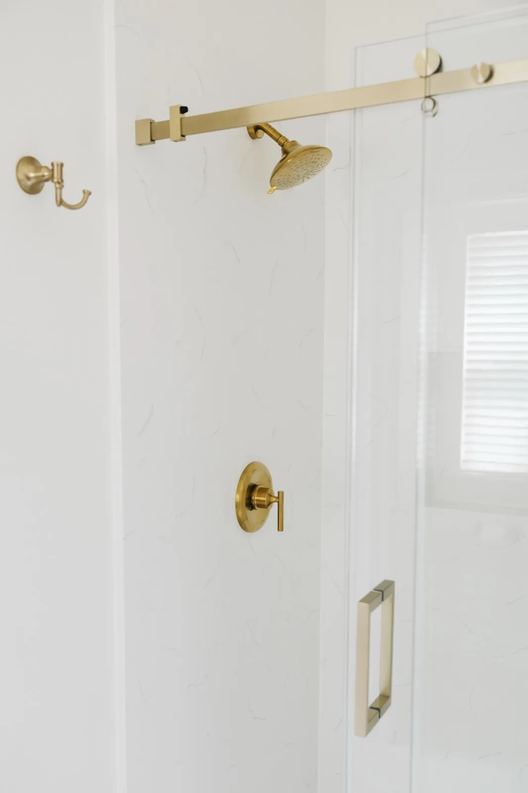 Shower from alternate angle — brass bar, showerhead, handle, and frameless glass