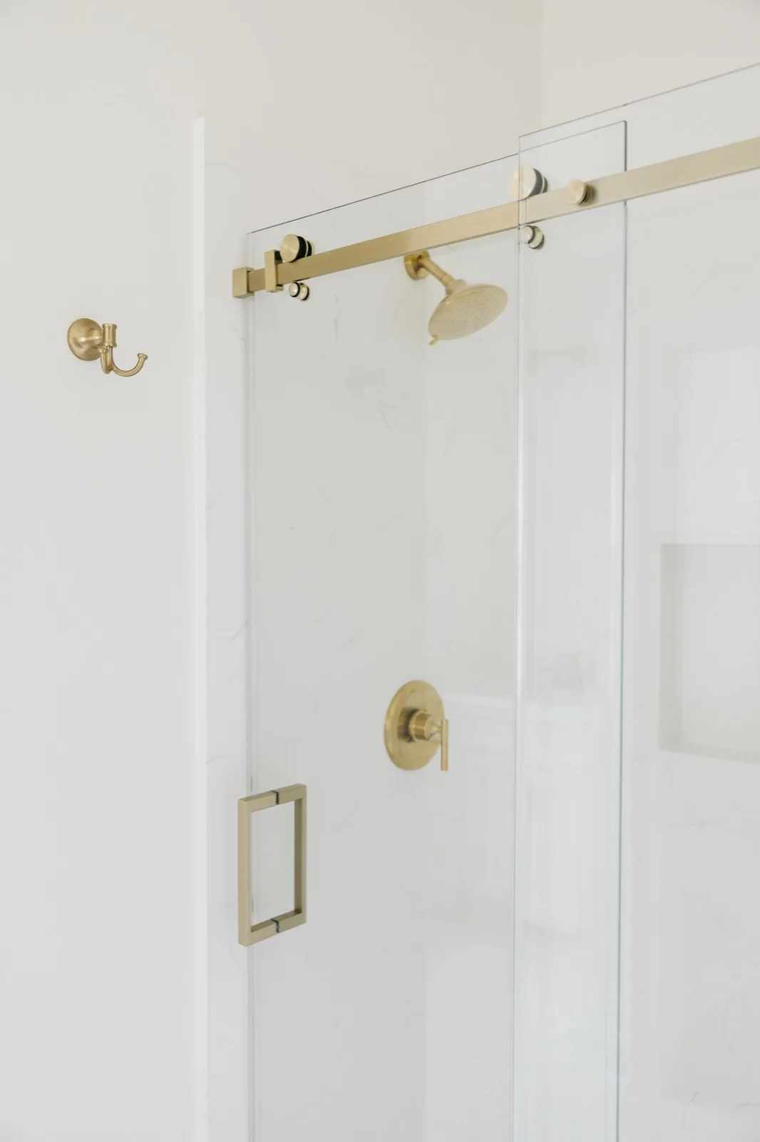 Shower hardware detail — brass sliding barn-door track, rain head, robe hook