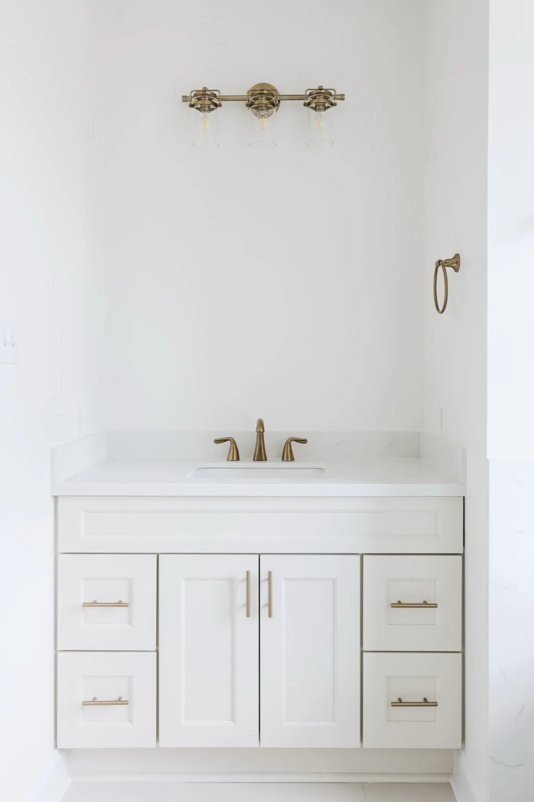 Bathroom vanity with brass faucet, industrial glass sconces, and towel ring