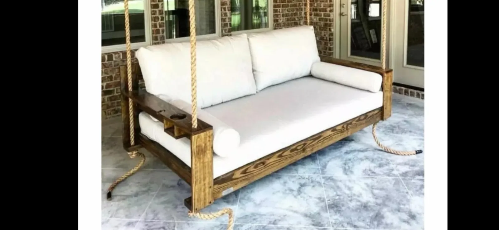 Dark-stained bed swing on covered porch with built-in cup holder tray and white cushions
