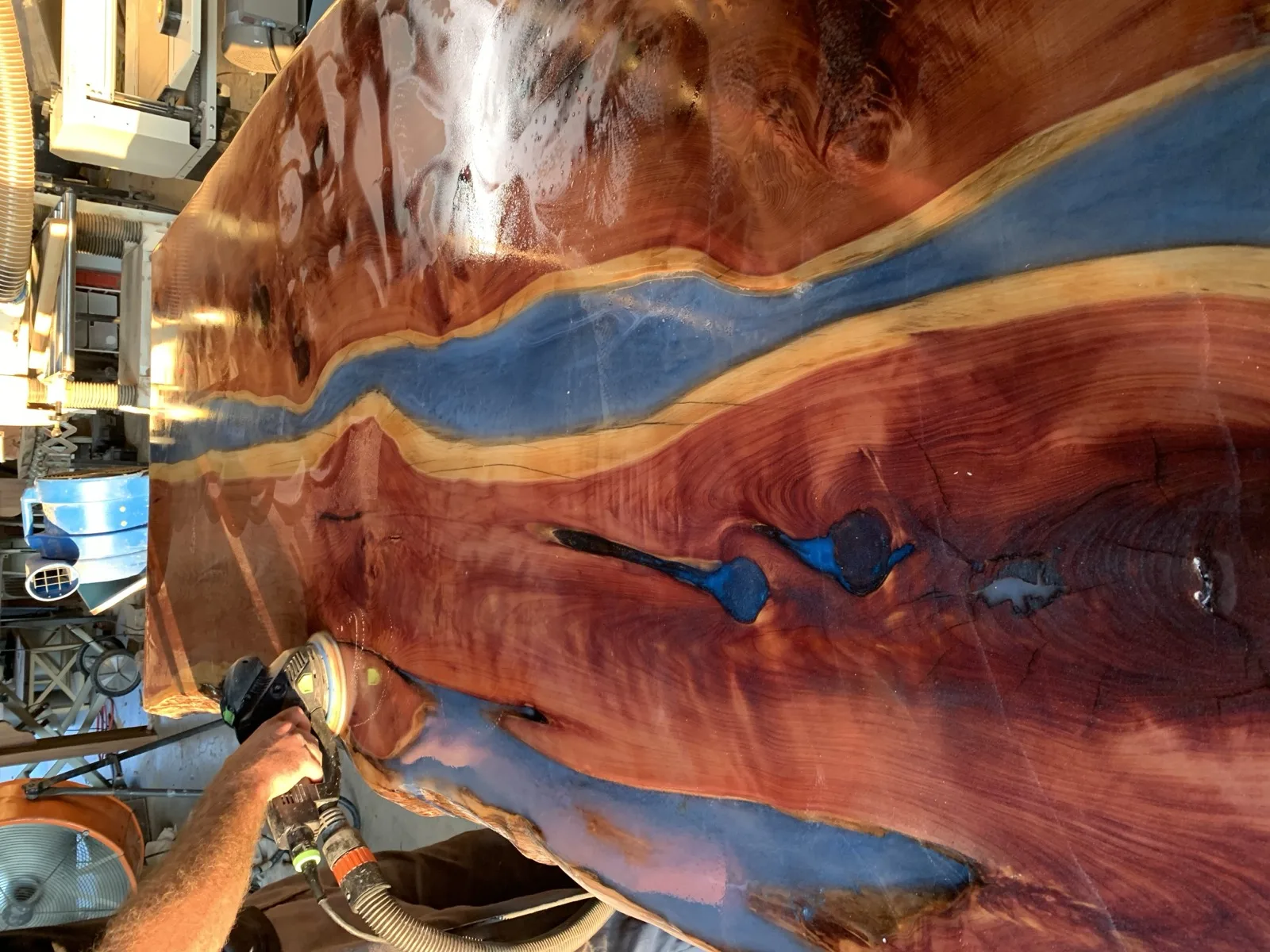 Sanding a red cedar slab with blue epoxy river — hand finishing in progress